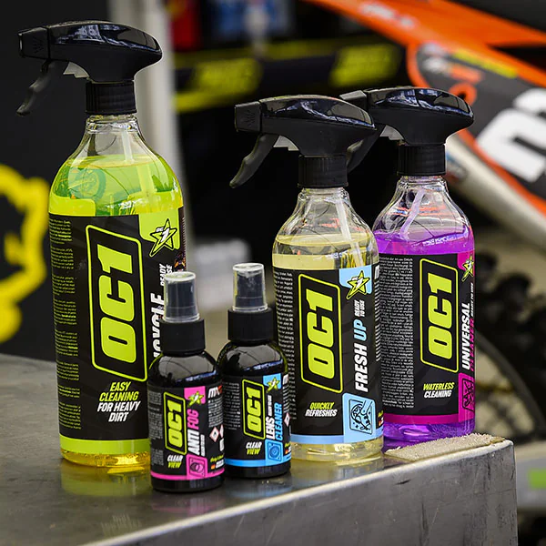 OC1 cleaning products on a workshop bench beside a motorcycle
